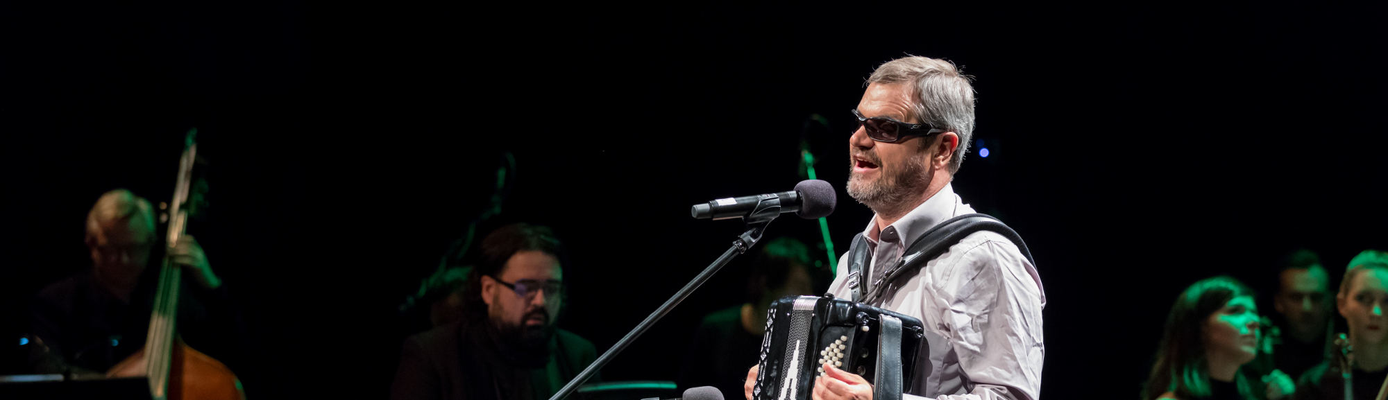 Photo de FaMo sur scène, chantant et jouant de l'accordéon, accompagné par le Sinfonieta Orchestra, au World Song Festival for the Blinds, à Cracovie, en 2017